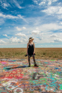 Krista Meadows stands on a colorfully spraypainted ground at Cadellac ranch just outside of Amarillo, Texas